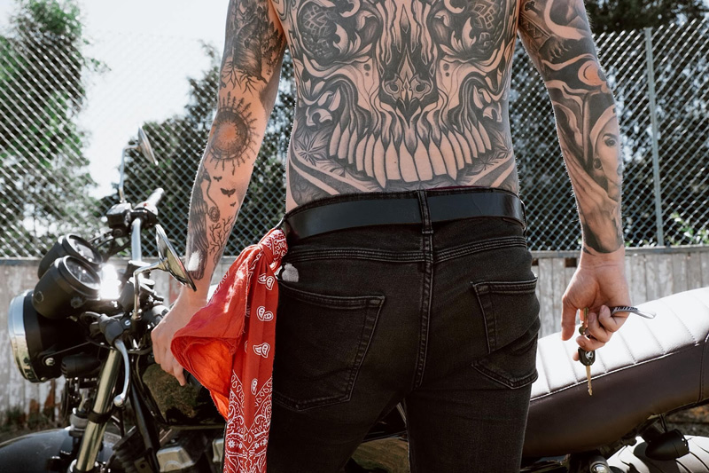 hombre con tatuajes en la espalda, caminando hacia una moto